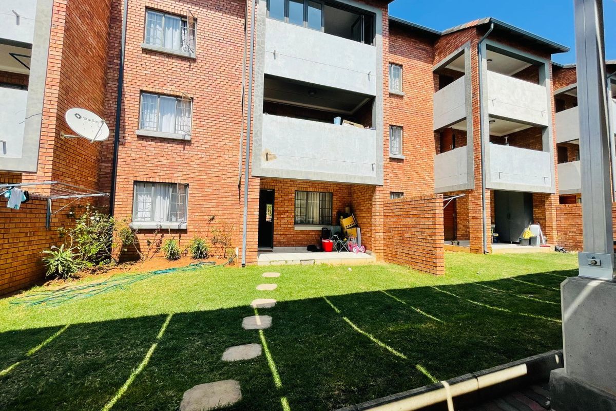 Rear view of a multi-story apartment complex featuring face brick facades, private balconies, and a shared garden area with a stone pathway.