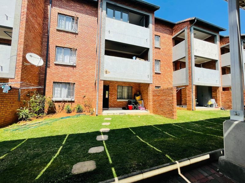 Rear view of a multi-story apartment complex featuring face brick facades, private balconies, and a shared garden area with a stone pathway.