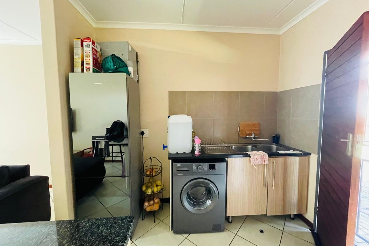 A compact kitchen area featuring tiled flooring, a double bowl sink with tiled splashback, and built-in cabinetry with space for a washing machine.