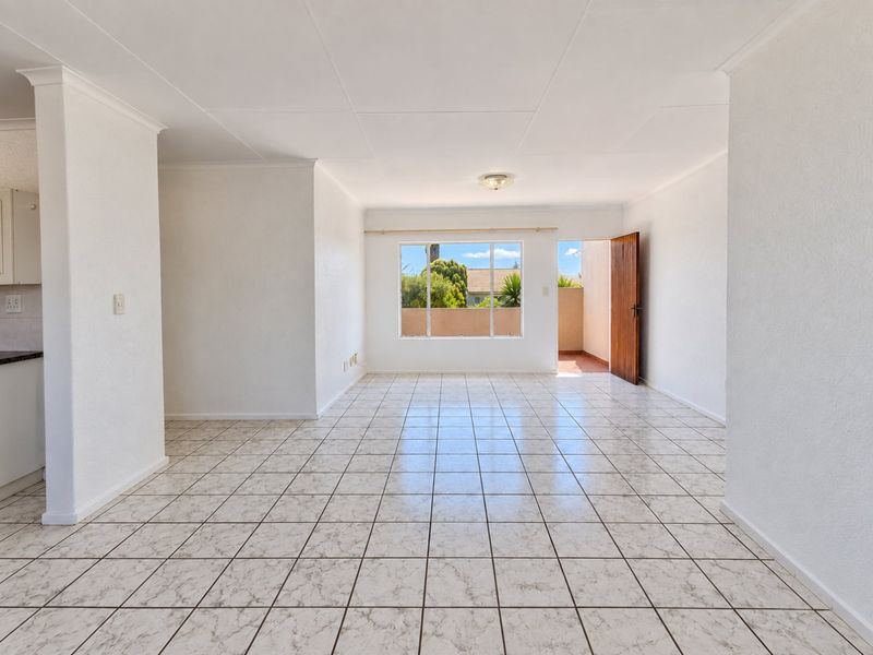 Spacious open-plan living area featuring neutral tiled flooring, clean white walls, and direct access to an outdoor balcony space.