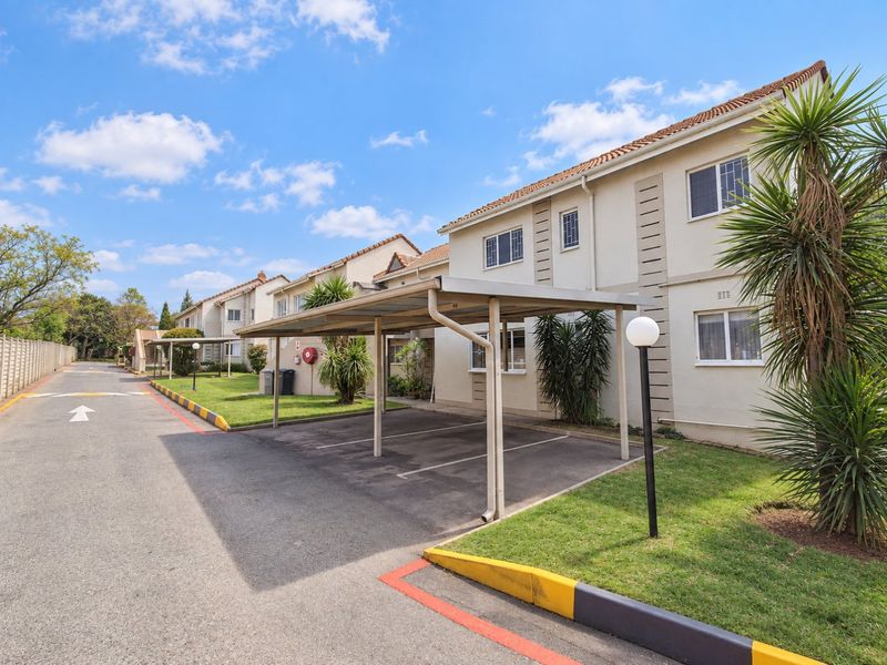 Exterior view of an apartment complex featuring covered parking bays, paved driveways, and well-maintained landscaped garden areas.