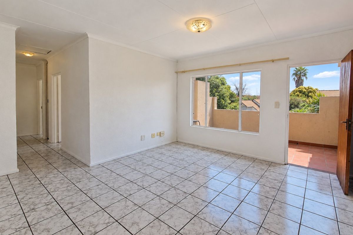 A bright, empty living area featuring neutral tiled flooring, clean white walls, and direct access to an outdoor balcony through a sliding door.