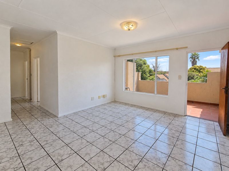 A bright, empty living area featuring neutral tiled flooring, clean white walls, and direct access to an outdoor balcony through a sliding door.
