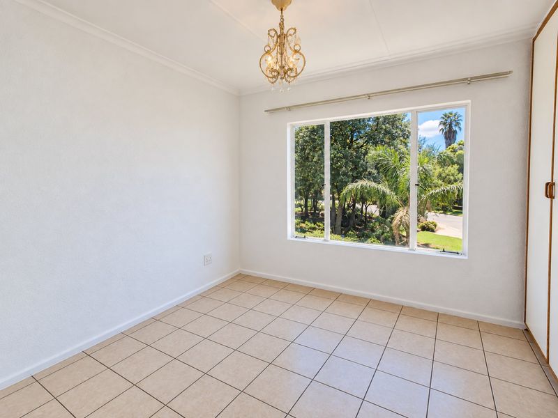 A bright, empty bedroom featuring tiled flooring, a built-in cupboard, and a large window with views of the surrounding greenery.