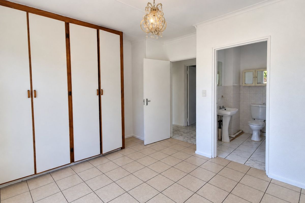 A spacious bedroom featuring built-in cupboards, tiled flooring, and an attached en-suite bathroom with a pedestal basin and toilet.