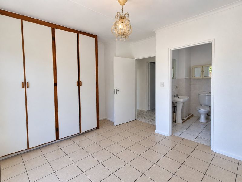 A spacious bedroom featuring built-in cupboards, tiled flooring, and an attached en-suite bathroom with a pedestal basin and toilet.