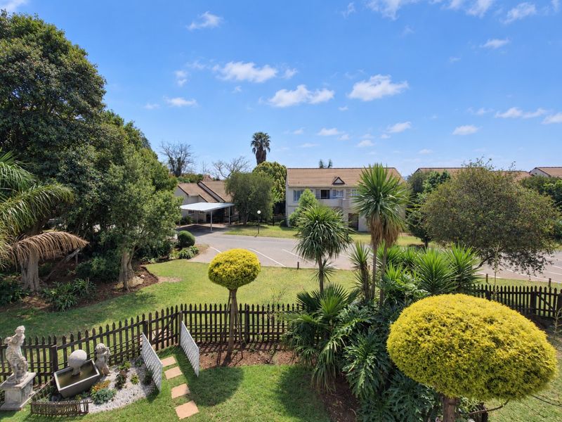 Elevated view overlooking a well-maintained communal garden, landscaped grounds, and residential parking area with carports.