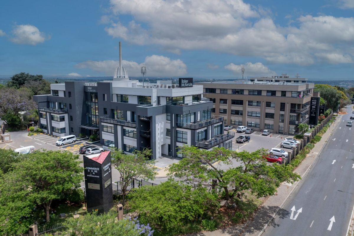 Aerial view of a modern commercial office complex featuring multiple buildings, paved parking, landscaped grounds, and prominent street-side signage.