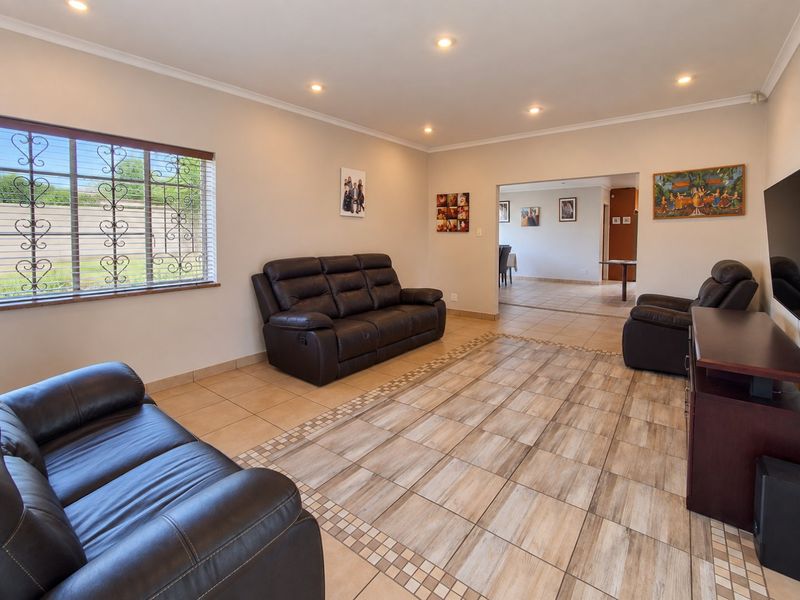 Spacious living room featuring neutral tiled flooring, recessed downlighting, and large windows with security bars, leading into an adjacent dining area.