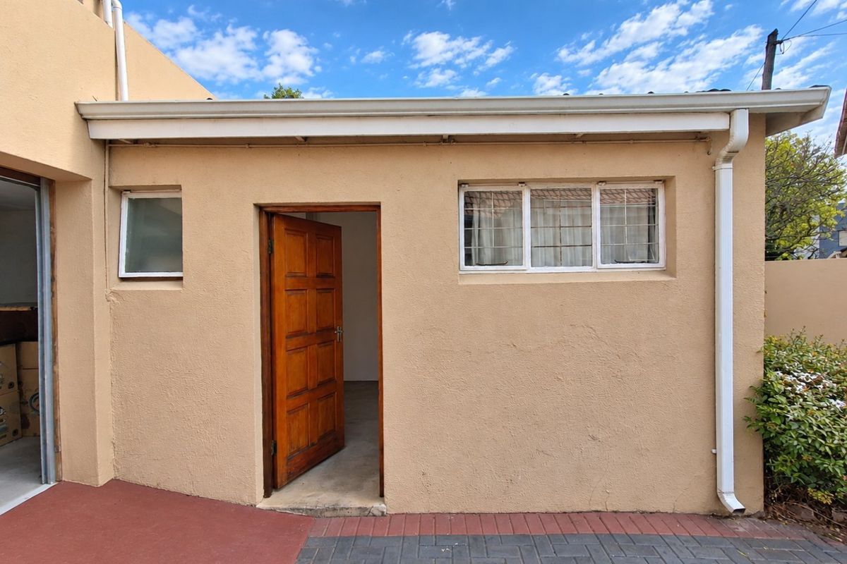 A rear exterior view of the property featuring a paved patio area, timber entrance door, and functional rainwater drainage system.