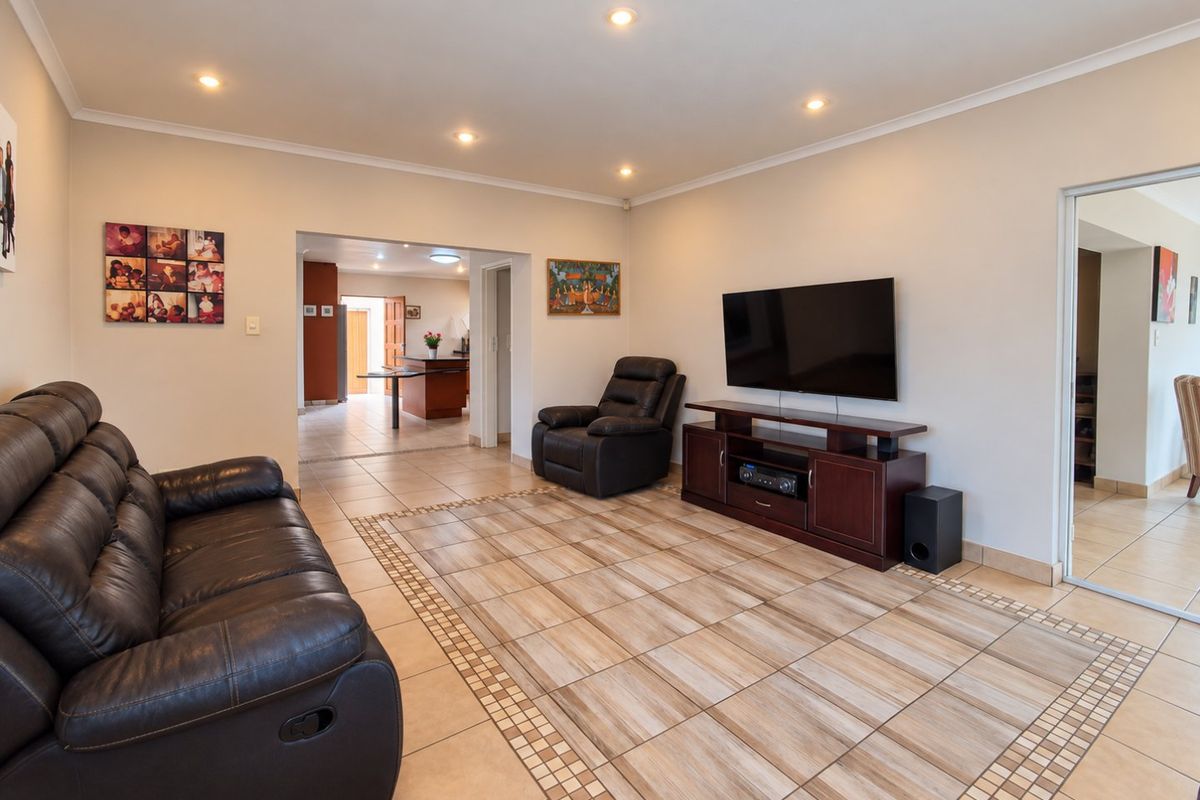 Spacious living room featuring neutral walls, recessed downlighting, and decorative tiled flooring with a border inlay, leading into an adjacent kitchen area.