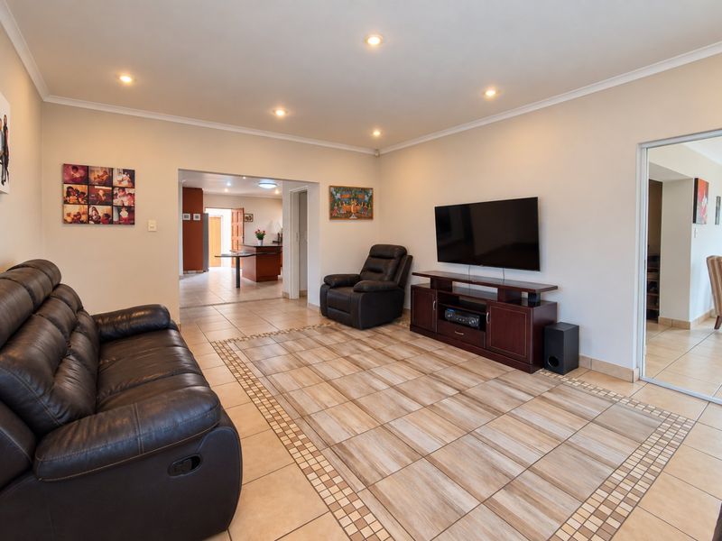 Spacious living room featuring neutral walls, recessed downlighting, and decorative tiled flooring with a border inlay, leading into an adjacent kitchen area.