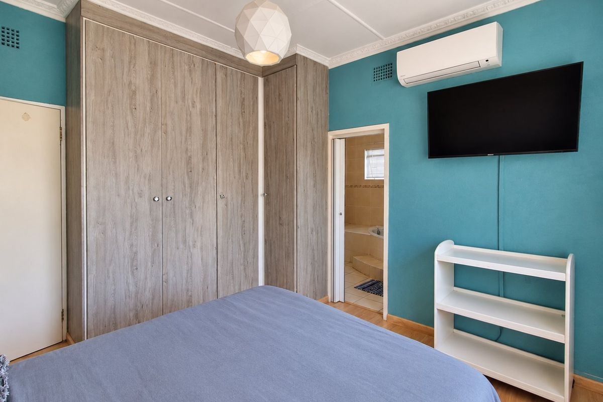 A well-maintained bedroom featuring built-in wood-grain cupboards, laminate flooring, a split-system air conditioner, and direct access to an en-suite bathroom.