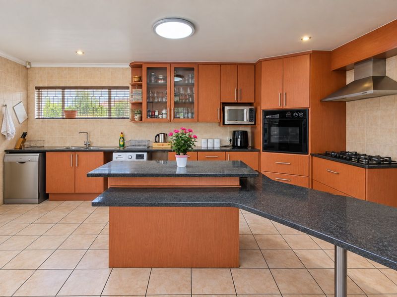 Spacious kitchen featuring warm-toned cabinetry, granite countertops, a central island, and integrated appliances, complemented by neutral tiled flooring and backsplash.