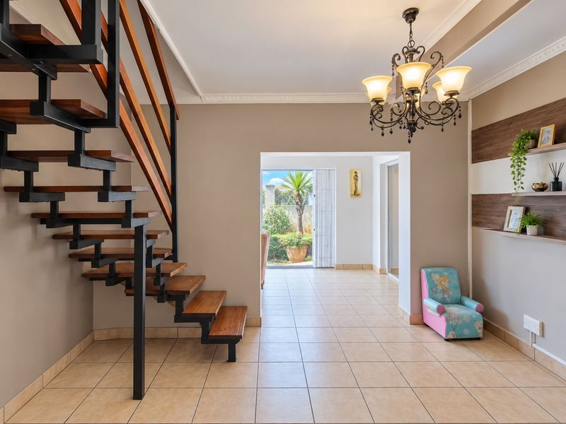 Welcoming entrance hall featuring a modern open-tread staircase with wooden steps, elegant chandelier lighting, and neutral tiled flooring leading toward the rear garden.