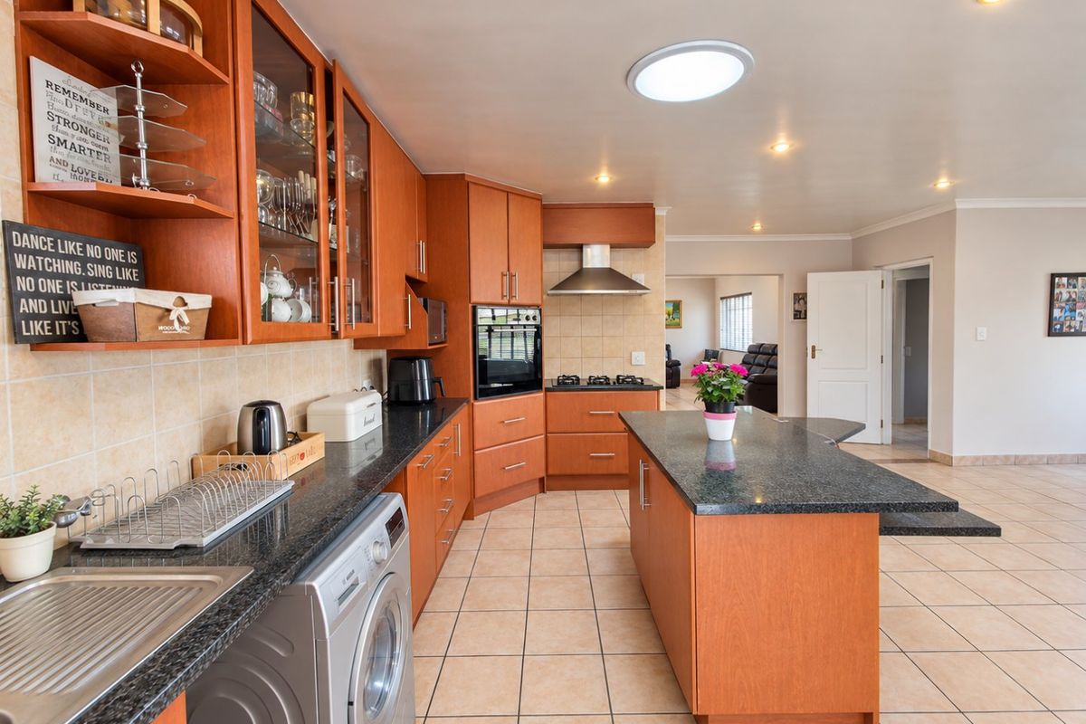 A spacious kitchen featuring warm wood cabinetry, granite countertops, a central island, and integrated appliances, flowing into an open-plan living area.
