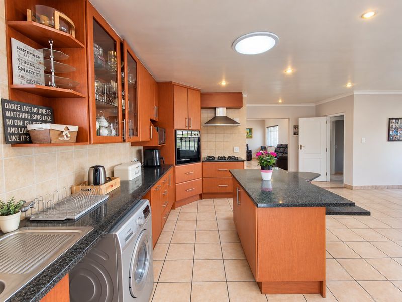 A spacious kitchen featuring warm wood cabinetry, granite countertops, a central island, and integrated appliances, flowing into an open-plan living area.