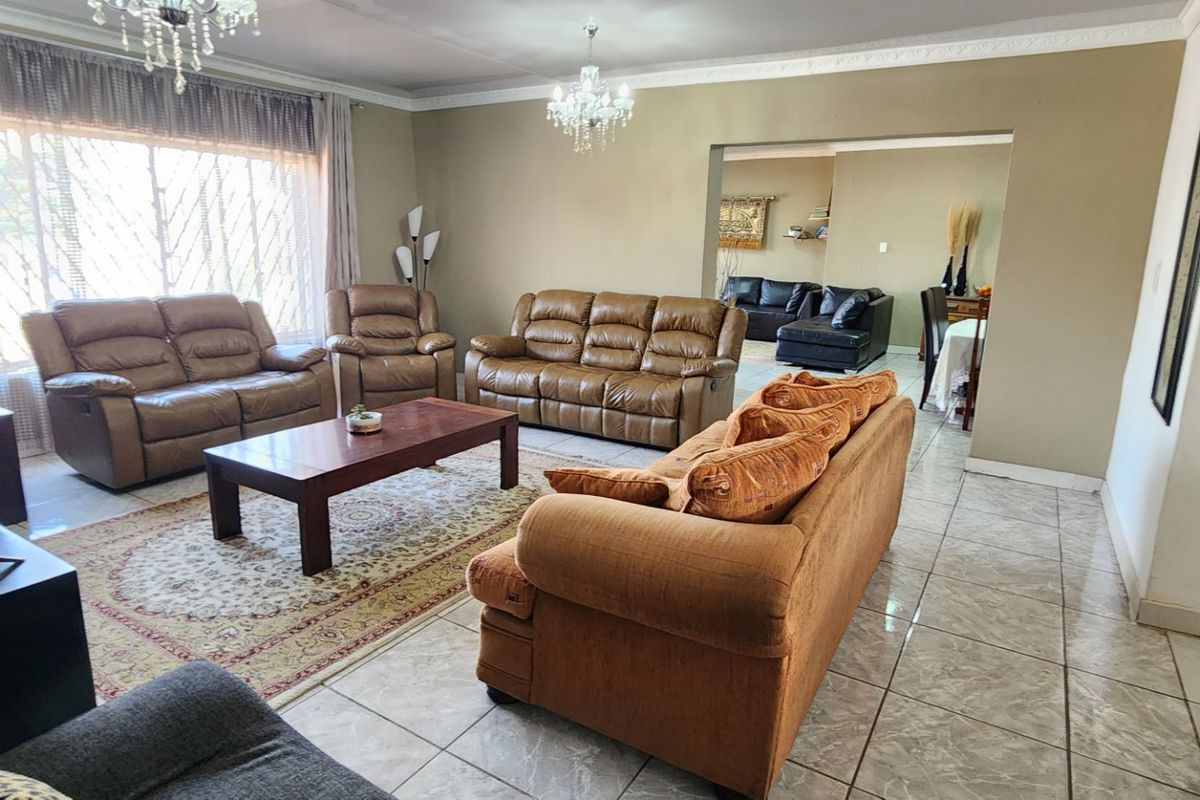 Spacious living room featuring tiled flooring, crown molding, and elegant crystal chandeliers, with an open-plan flow into the adjacent dining area.