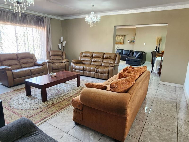 Spacious living room featuring tiled flooring, crown molding, and elegant crystal chandeliers, with an open-plan flow into the adjacent dining area.
