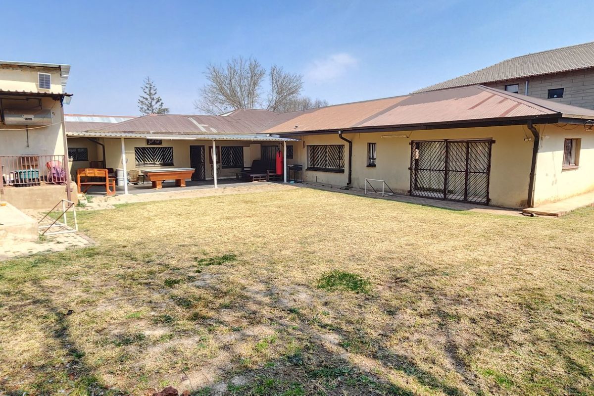 Rear view of the property featuring a covered patio area, security gates, and a spacious backyard with established lawn.