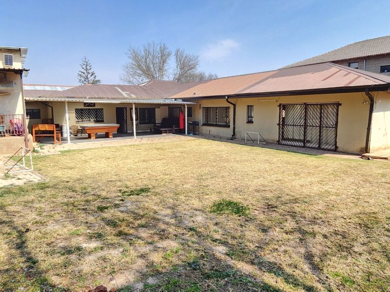 Rear view of the property featuring a covered patio area, security gates, and a spacious backyard with established lawn.