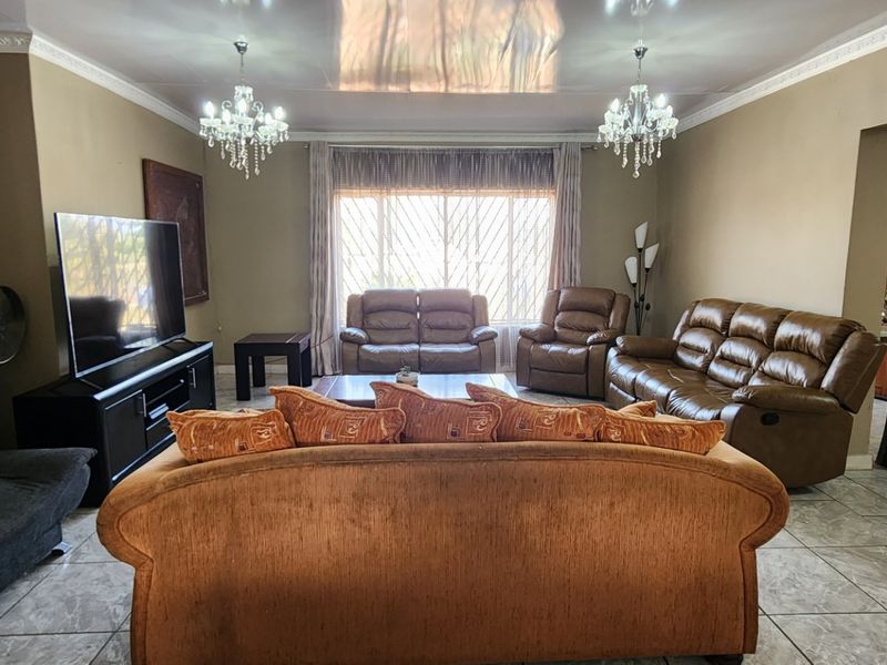 Spacious living room featuring tiled flooring, decorative ceiling molding, and dual crystal chandeliers, providing a comfortable and well-lit area for relaxation.