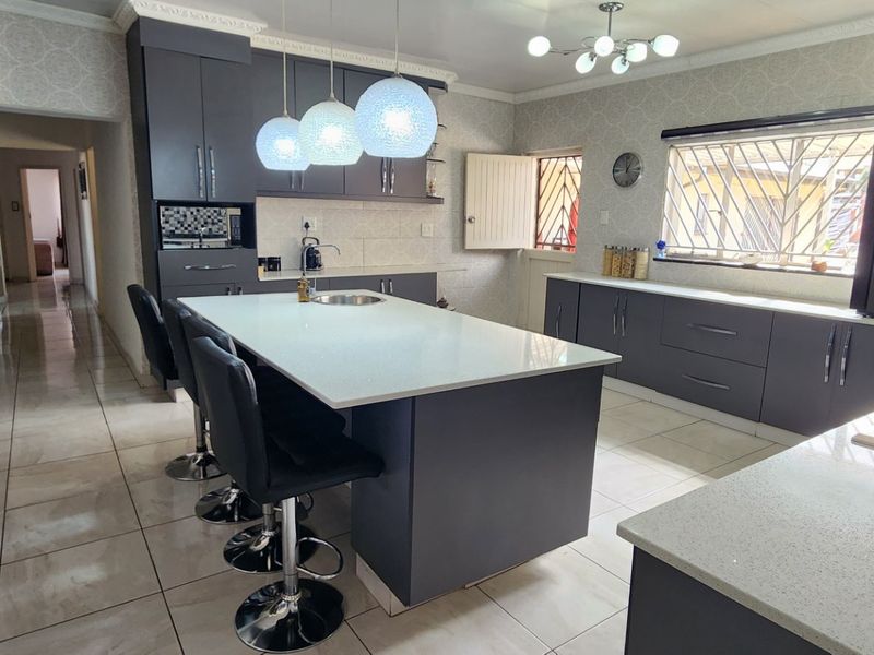 Modern kitchen featuring dark grey cabinetry, white quartz countertops, a central island with seating, and a gas hob, finished with tiled flooring.
