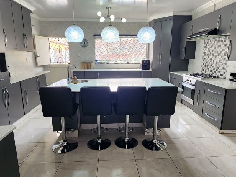 Modern kitchen featuring dark grey cabinetry, a central island with seating, quartz countertops, built-in gas hob, oven, and tiled flooring.