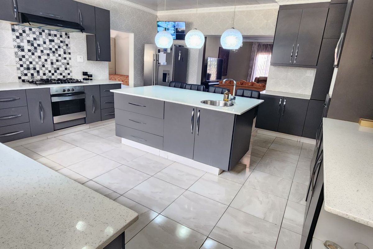 Modern kitchen featuring dark grey cabinetry, a central island with a sink, quartz countertops, and tiled flooring.