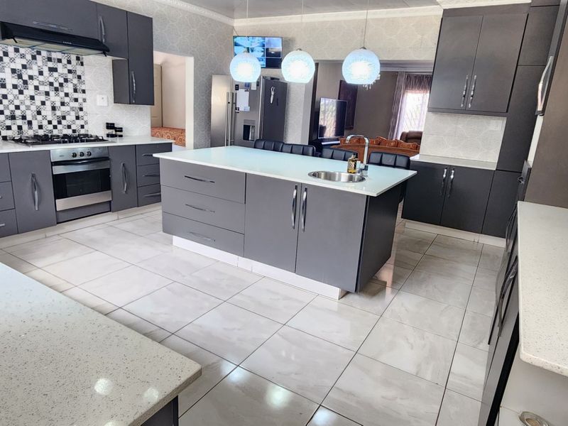 Modern kitchen featuring dark grey cabinetry, a central island with a sink, quartz countertops, and tiled flooring.