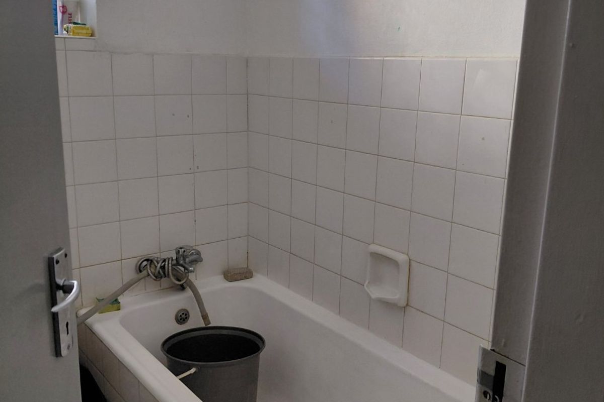 A functional bathroom featuring a standard bathtub with wall-mounted faucet and tiled splashback, requiring minor maintenance and cosmetic updates.