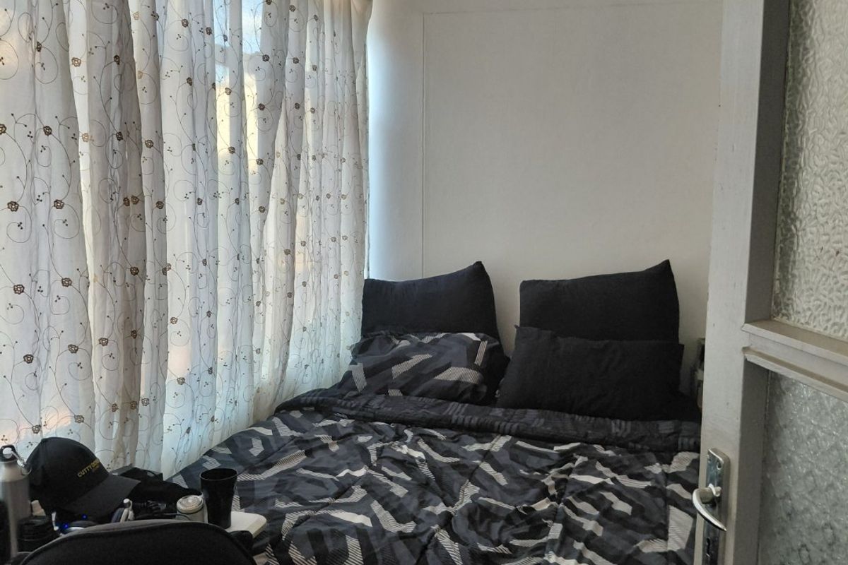 A compact bedroom featuring a large window with curtains and a classic internal door with a glass panel.