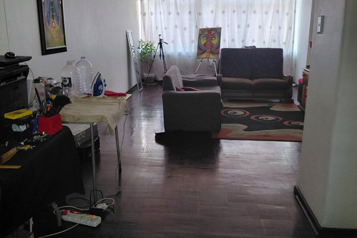 A living room featuring dark parquet flooring and a large window with curtains, providing natural light to the space.