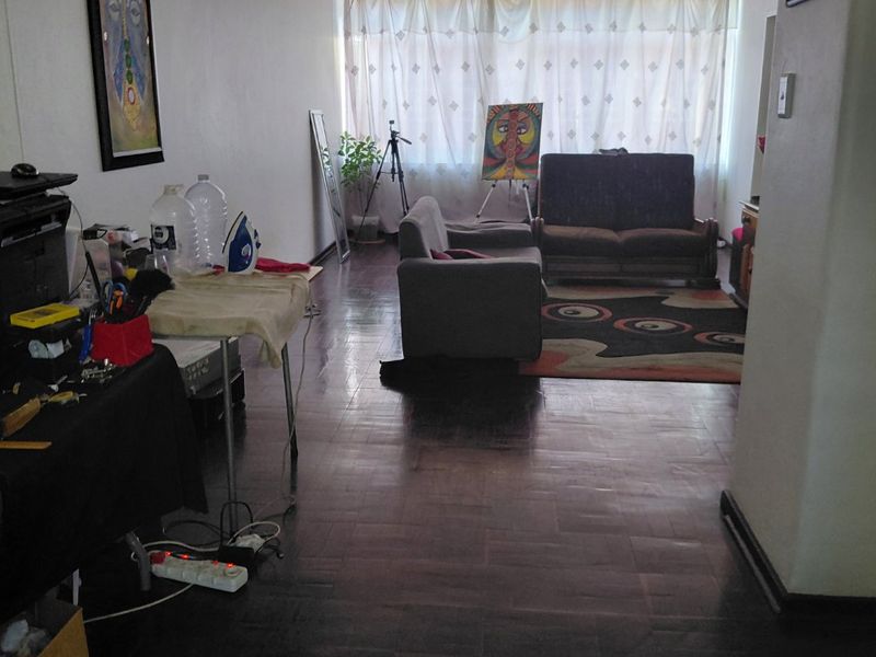 A living room featuring dark parquet flooring and a large window with curtains, providing natural light to the space.