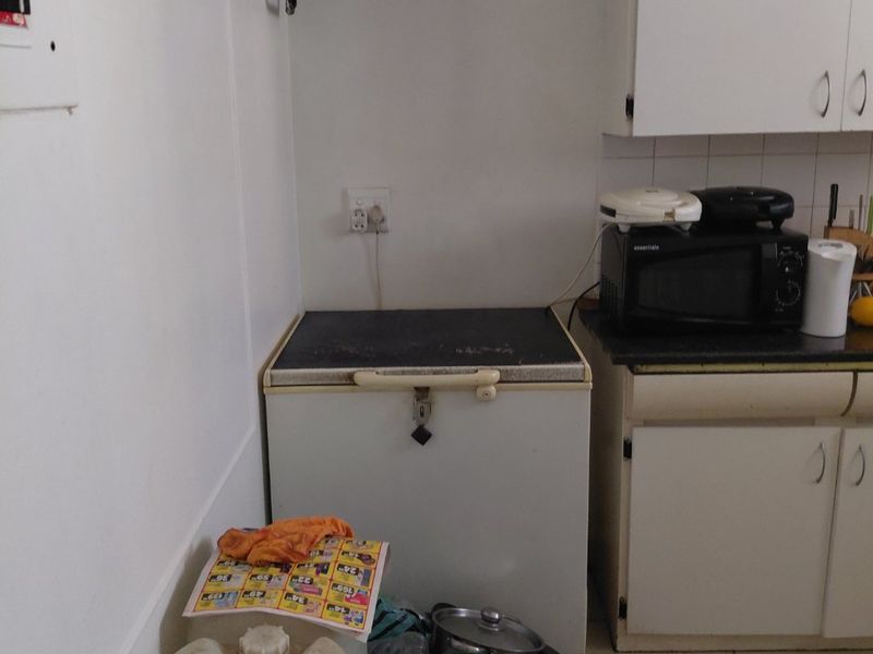 A compact kitchen area featuring white built-in cabinetry, tiled flooring, and a laminate countertop, currently used for storage and appliance placement.