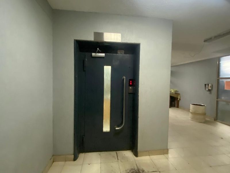 A functional apartment building hallway featuring tiled flooring and an elevator access point with a metal door.