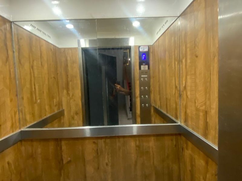 Interior view of an apartment building elevator featuring wood-paneled walls, a large mirror, and stainless steel accents.