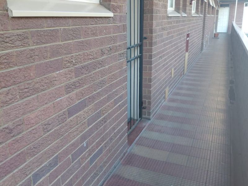 An exterior apartment hallway featuring brick walls, tiled flooring, and security gates for unit access.