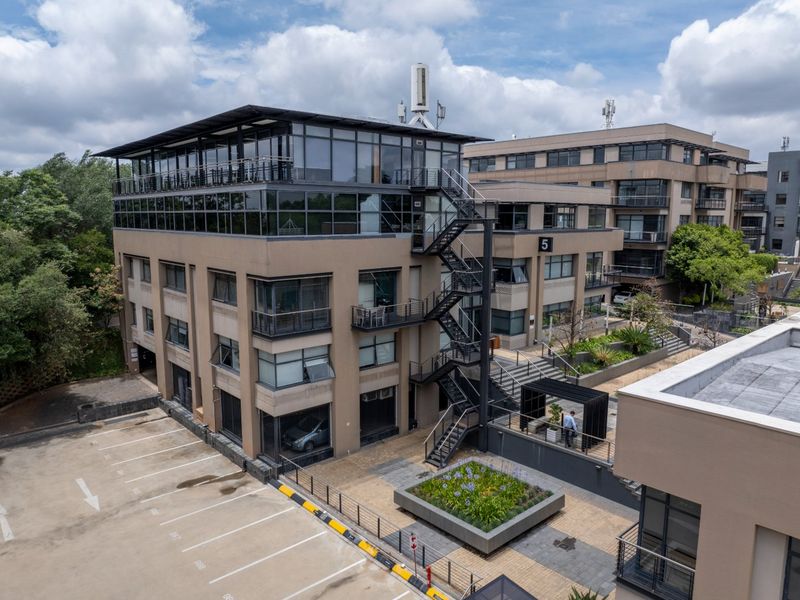 Aerial view of a multi-story commercial office building featuring glass facades, external fire escape stairs, and an adjacent paved parking area.