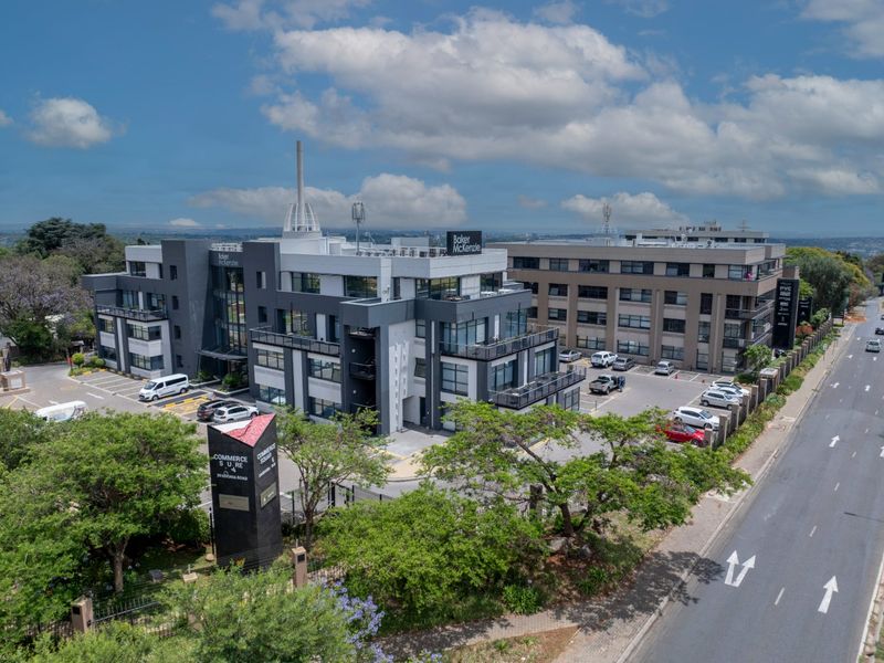 Aerial view of a modern commercial office complex featuring multiple buildings, paved parking, landscaped grounds, and prominent street-side signage.