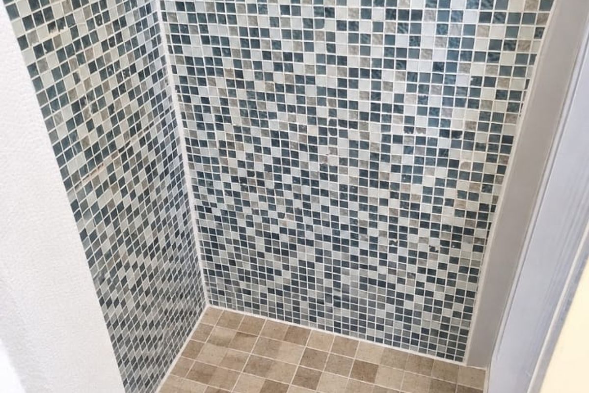 A walk-in shower enclosure featuring decorative mosaic wall tiling and neutral floor tiles with a central drain.