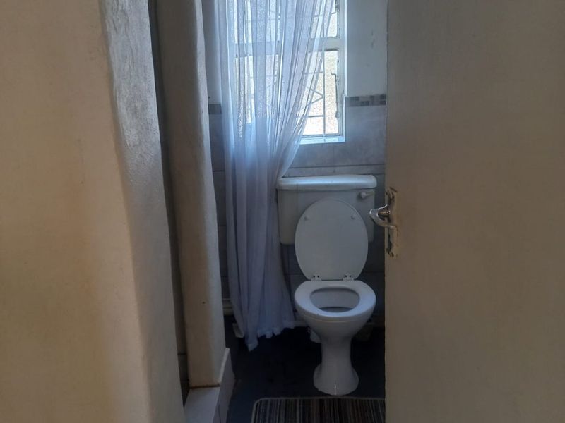 A small, functional bathroom featuring a standard toilet and a window with security bars, requiring cosmetic updates to improve its overall condition.