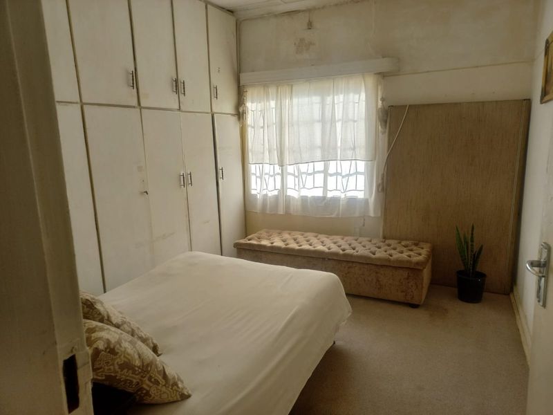 A bedroom featuring extensive built-in cupboards and carpeted flooring, currently requiring cosmetic updates to the walls and ceiling to improve its overall condition.