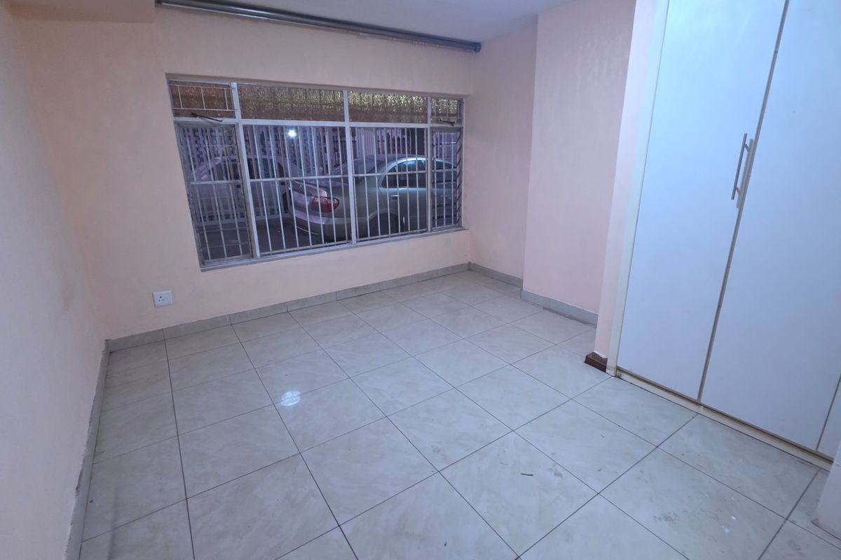 An empty bedroom featuring tiled flooring, built-in cupboards, and a window fitted with security bars.