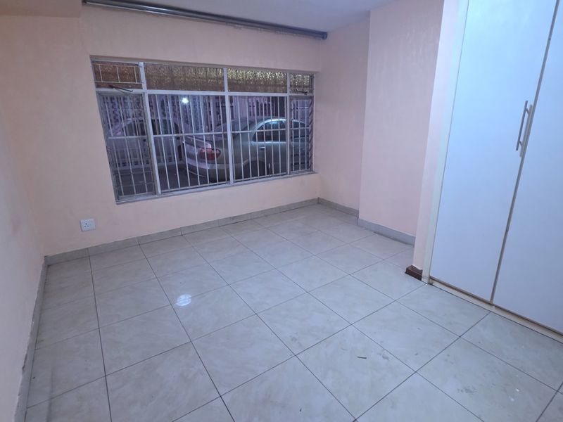 An empty bedroom featuring tiled flooring, built-in cupboards, and a window fitted with security bars.