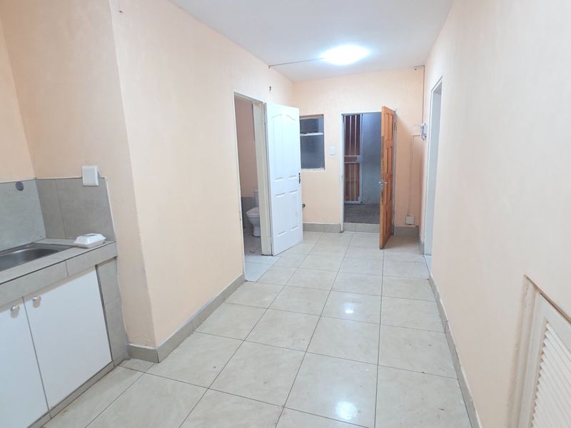 An open-plan kitchen area featuring tiled flooring, built-in cabinetry, and a sink, providing access to adjacent rooms.
