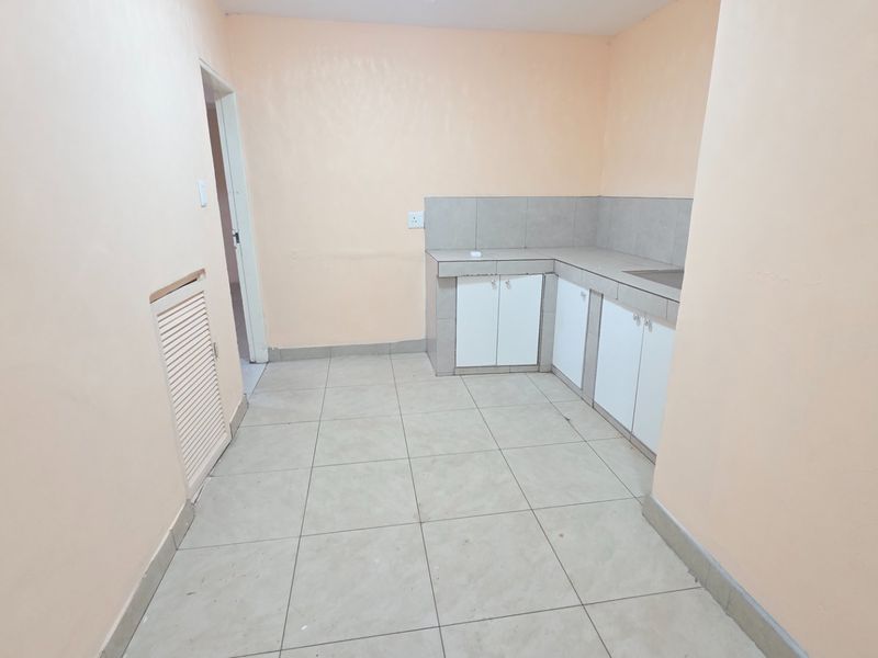 A compact, empty kitchen featuring tiled flooring, built-in base cabinetry with a tiled splashback, and a functional sink area.