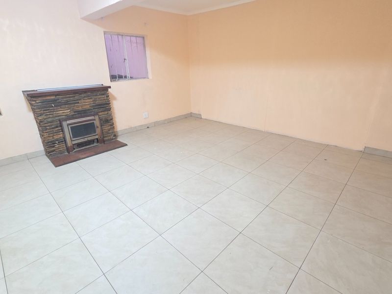 An empty living room featuring tiled flooring and a stone-clad fireplace, offering a blank canvas for renovation and interior design updates.