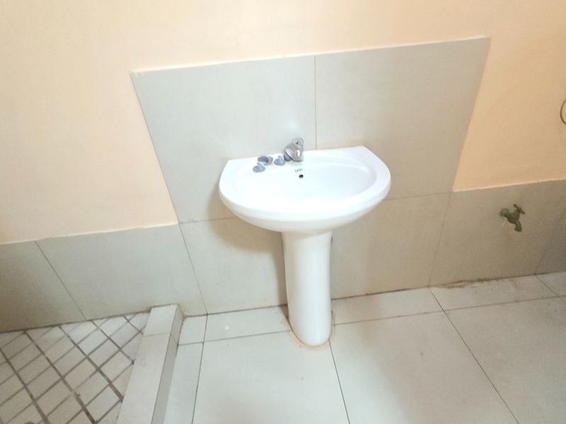 A functional bathroom featuring a white pedestal basin, ceramic wall and floor tiling, and a standard toilet fixture.