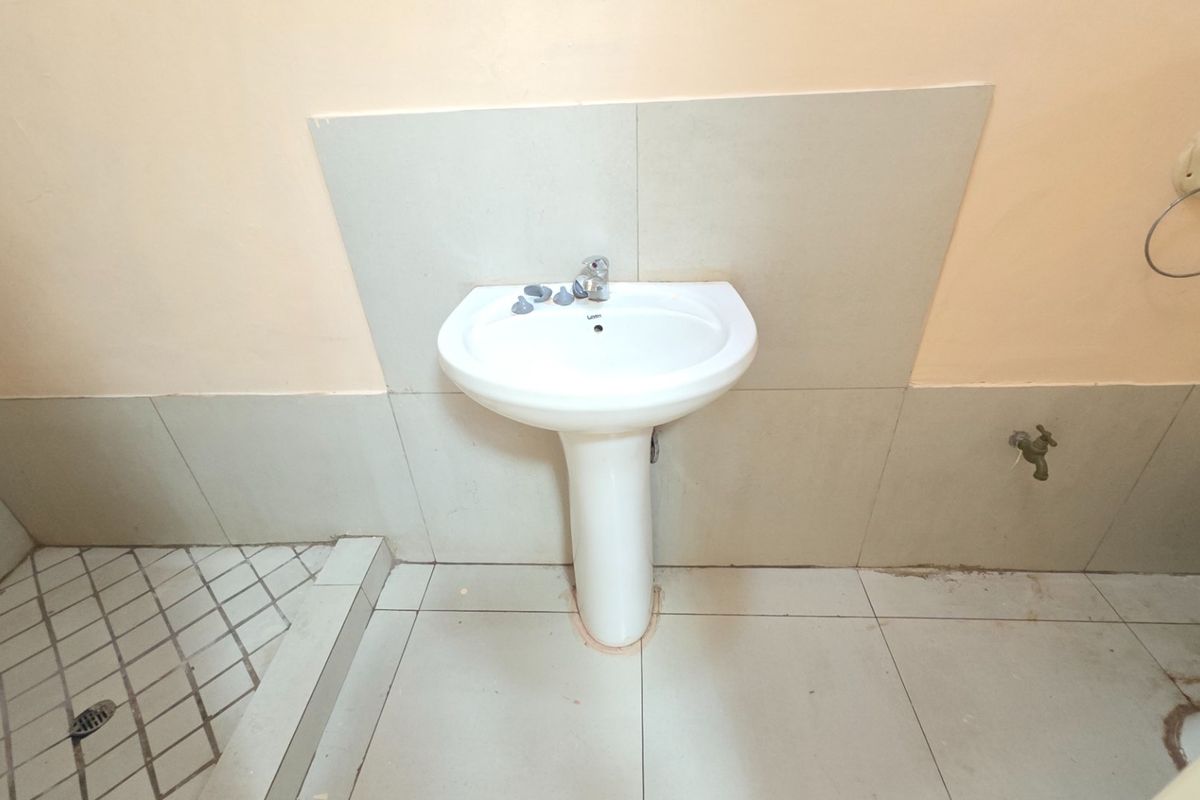 A functional bathroom featuring a white pedestal basin, tiled splashback, and neutral floor tiling, presenting a basic and dated aesthetic.